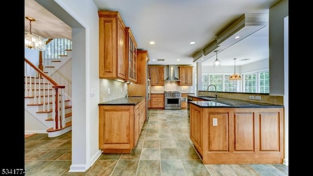 kitchen with a sink, stainless steel range oven, brown cabinets, and wall chimney exhaust hood