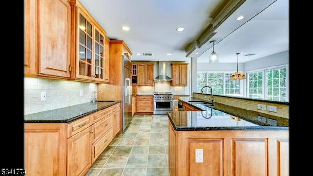 kitchen featuring a sink, premium appliances, wall chimney exhaust hood, and dark stone countertops