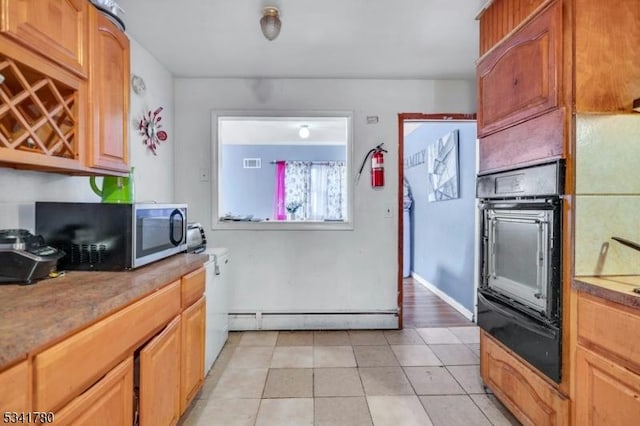 kitchen with light tile patterned floors, a baseboard radiator, oven, stainless steel microwave, and a warming drawer