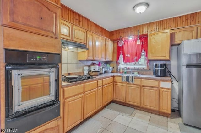 kitchen with wall oven, under cabinet range hood, light countertops, freestanding refrigerator, and gas stovetop