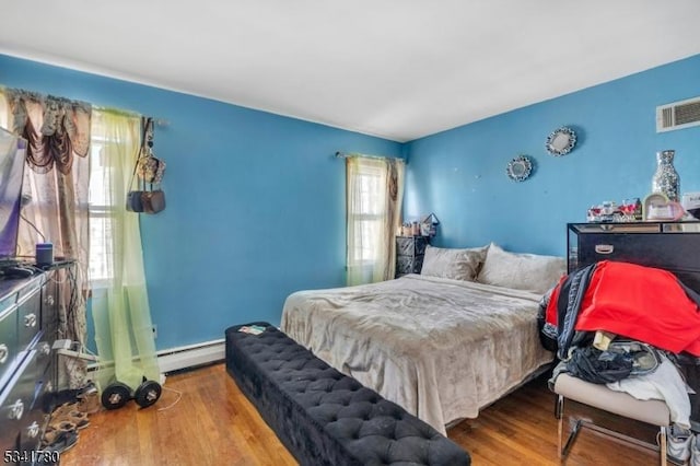 bedroom with baseboard heating, visible vents, and wood finished floors