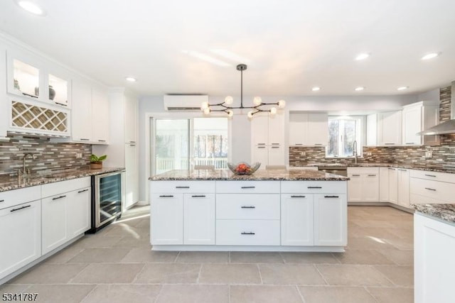 kitchen featuring a wall unit AC, backsplash, white cabinets, a sink, and beverage cooler