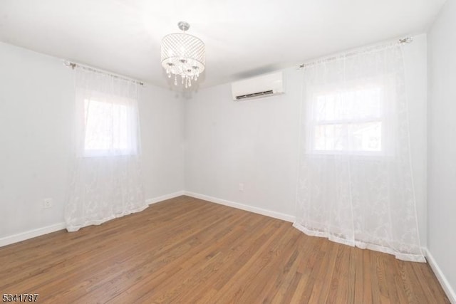 unfurnished room with an AC wall unit, plenty of natural light, wood finished floors, and an inviting chandelier