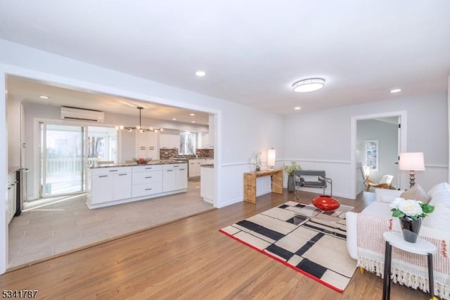 living area featuring recessed lighting, baseboards, light wood-type flooring, a wall mounted air conditioner, and an inviting chandelier