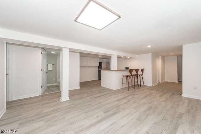 finished below grade area with baseboards, recessed lighting, fridge, and light wood-style floors