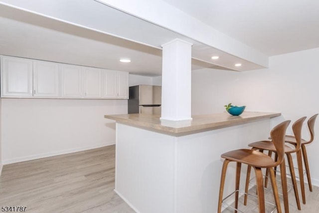 kitchen with recessed lighting, light wood-style flooring, freestanding refrigerator, white cabinetry, and a kitchen bar