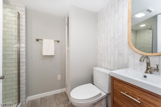 full bathroom with toilet, wood finished floors, vanity, baseboards, and a tile shower