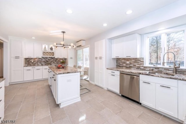 kitchen featuring tasteful backsplash, stainless steel dishwasher, an AC wall unit, white cabinetry, and a sink