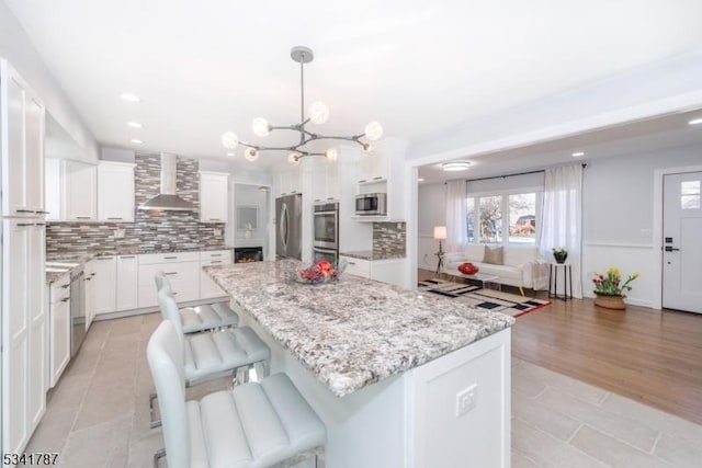 kitchen featuring tasteful backsplash, a center island, stainless steel appliances, wall chimney range hood, and white cabinetry