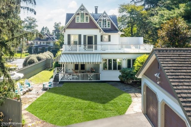 rear view of house with a yard, a balcony, and fence