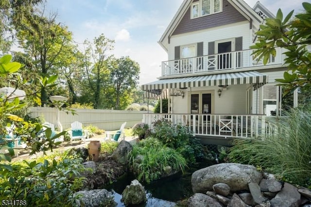 rear view of house featuring a balcony, fence, a porch, and french doors