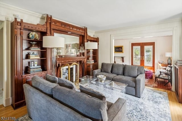 living area with light wood-style floors, a fireplace, ornamental molding, and french doors