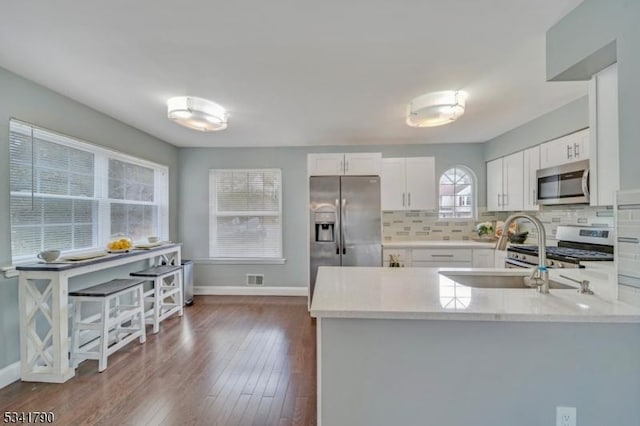 kitchen with baseboards, a peninsula, stainless steel appliances, decorative backsplash, and white cabinetry