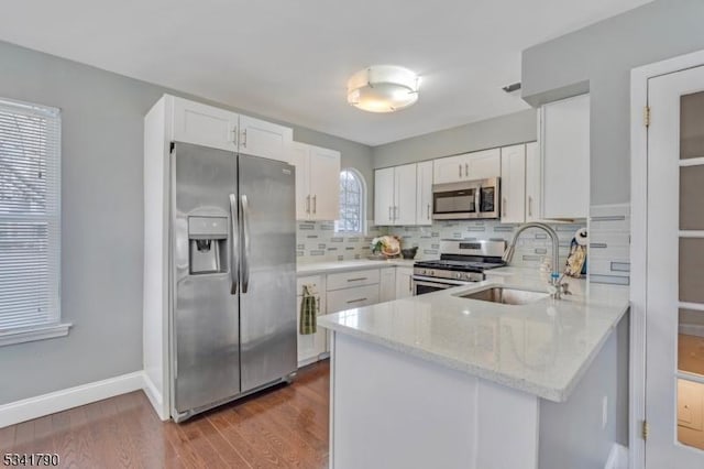 kitchen featuring a peninsula, a sink, decorative backsplash, stainless steel appliances, and white cabinets