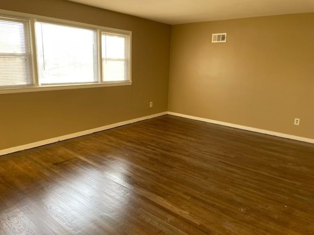 empty room featuring baseboards, visible vents, and dark wood-style flooring