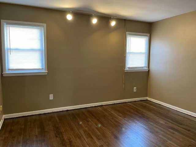 empty room featuring rail lighting, baseboards, and wood finished floors