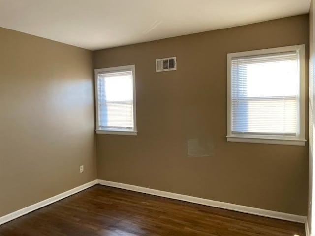 spare room with dark wood finished floors, visible vents, and baseboards