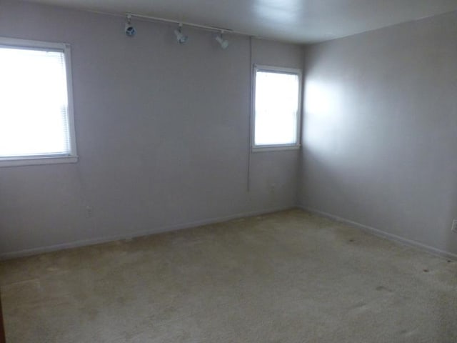 spare room featuring carpet floors, rail lighting, and baseboards