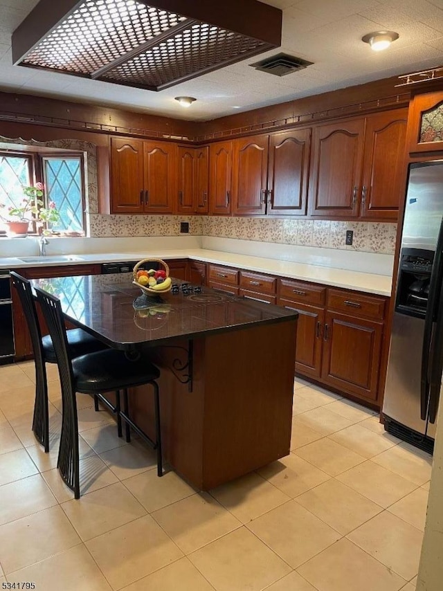 kitchen featuring a breakfast bar, a kitchen island, visible vents, stainless steel fridge with ice dispenser, and decorative backsplash