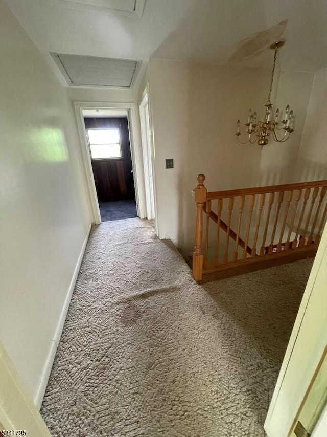 hall with carpet floors, an inviting chandelier, attic access, an upstairs landing, and baseboards