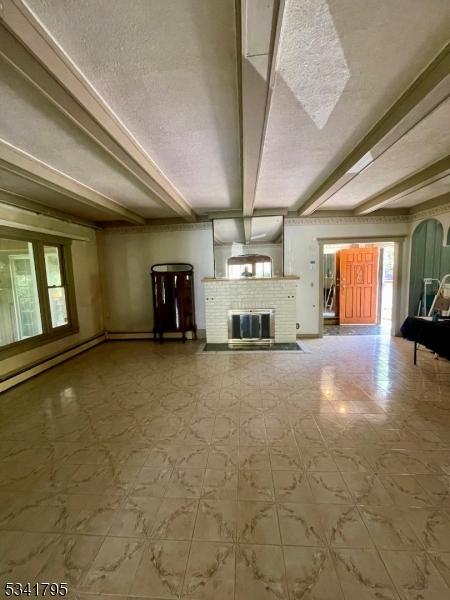 unfurnished living room with a fireplace, beamed ceiling, and tile patterned floors