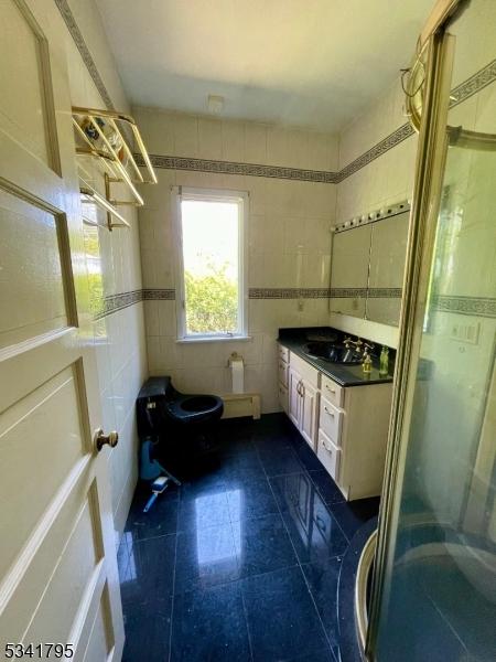 full bathroom with toilet, a stall shower, tile walls, and vanity