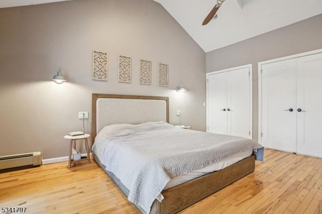 bedroom featuring high vaulted ceiling, a baseboard radiator, wood-type flooring, and multiple closets