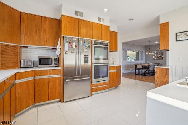 kitchen with visible vents, appliances with stainless steel finishes, brown cabinets, light countertops, and backsplash