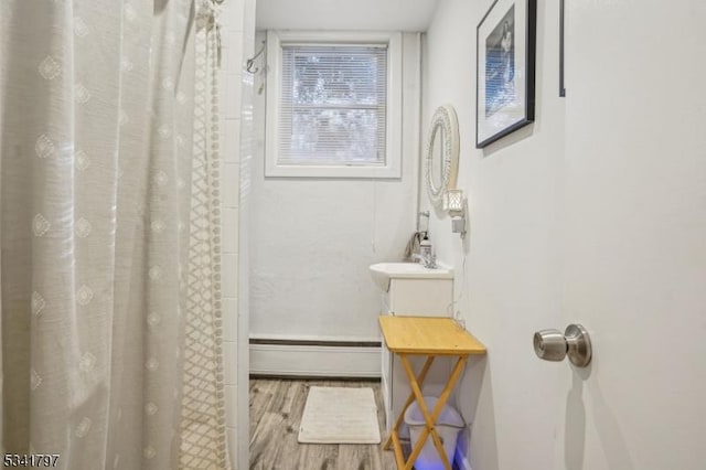 full bathroom with a shower with shower curtain, vanity, baseboard heating, and wood finished floors