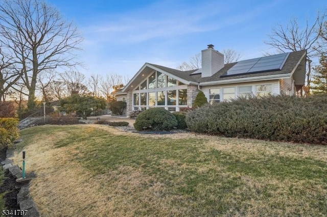 back of house with roof mounted solar panels, a lawn, and a chimney