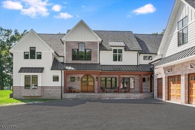 view of front facade featuring driveway, brick siding, a standing seam roof, and board and batten siding