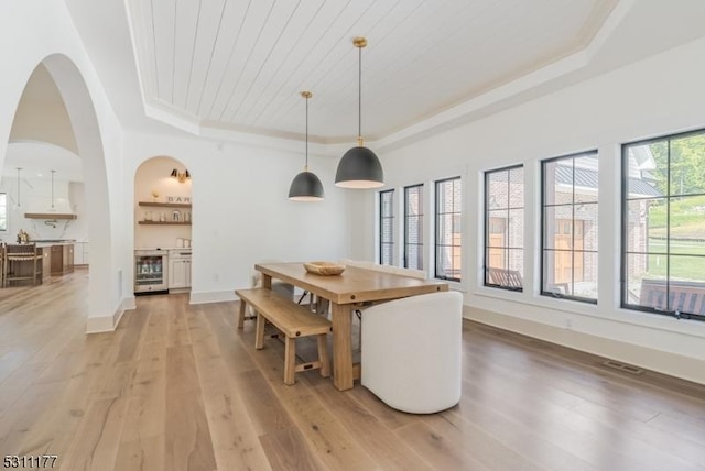 dining space with baseboards, visible vents, light wood-style flooring, wine cooler, and a tray ceiling