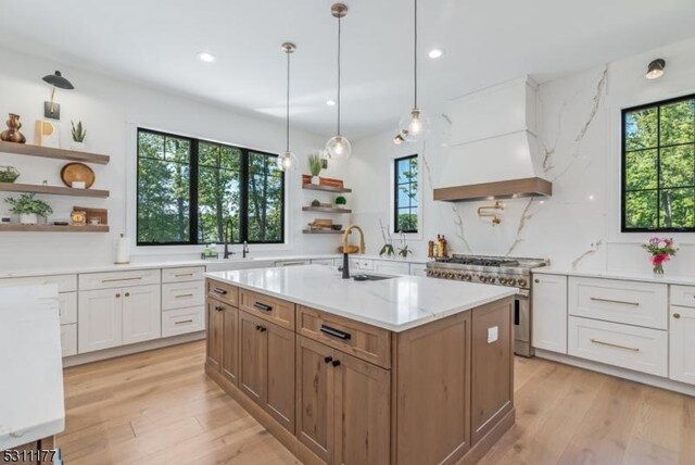 kitchen with light wood finished floors, range with two ovens, custom range hood, open shelves, and a sink