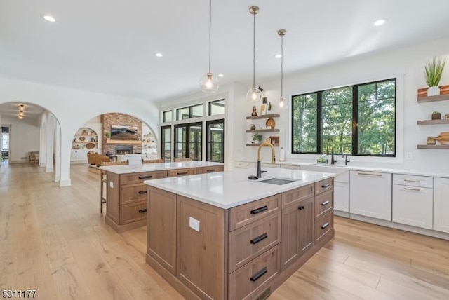 kitchen with arched walkways, a kitchen island with sink, a sink, and open shelves