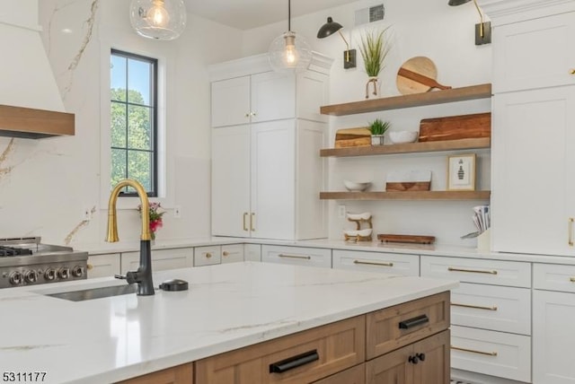 kitchen featuring visible vents, premium range hood, white cabinetry, open shelves, and a sink