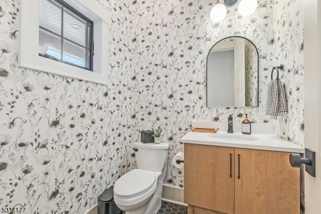 bathroom with toilet, wallpapered walls, and vanity