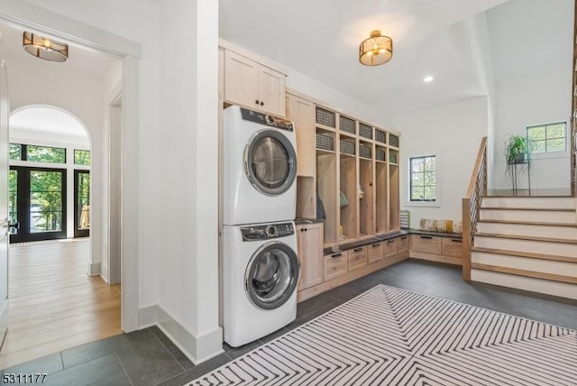 laundry area with stacked washing maching and dryer, baseboards, arched walkways, and a wealth of natural light