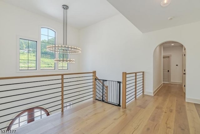 hall with arched walkways, a notable chandelier, wood finished floors, an upstairs landing, and baseboards