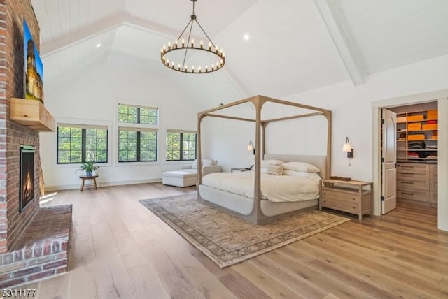 unfurnished bedroom with beam ceiling, a fireplace, a spacious closet, wood finished floors, and high vaulted ceiling