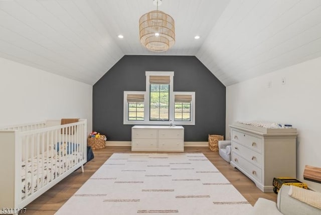 bedroom featuring recessed lighting, wood finished floors, baseboards, vaulted ceiling, and a nursery area