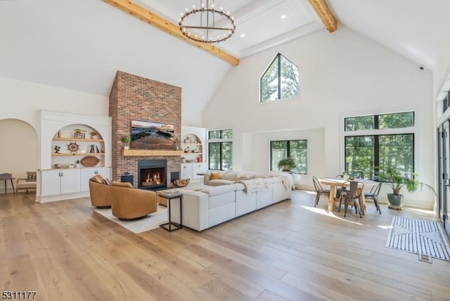 living room featuring light wood-style floors, beamed ceiling, a brick fireplace, high vaulted ceiling, and a notable chandelier