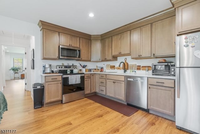 kitchen featuring light wood-style flooring, stainless steel appliances, a sink, and light countertops