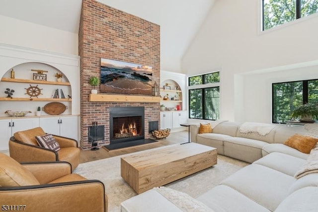 living room with built in features, light wood-type flooring, a fireplace, and high vaulted ceiling