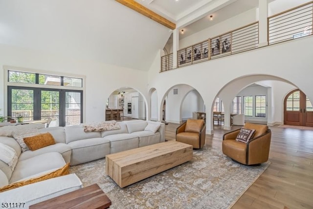 living area featuring arched walkways, wood finished floors, beamed ceiling, a high ceiling, and french doors