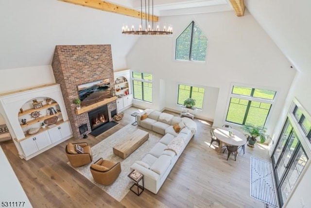 living area with a healthy amount of sunlight, a brick fireplace, a notable chandelier, and wood finished floors