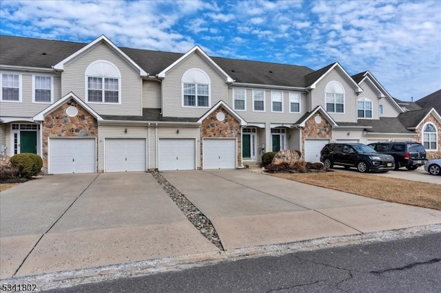 townhome / multi-family property with a garage, driveway, and stone siding