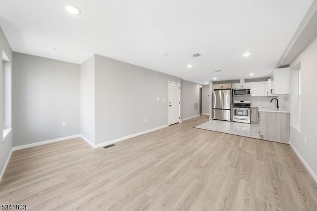 unfurnished living room with recessed lighting, a sink, visible vents, baseboards, and light wood-type flooring