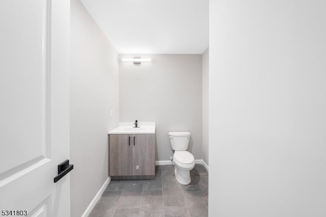 half bath featuring tile patterned flooring, vanity, toilet, and baseboards