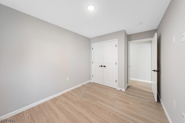 unfurnished bedroom with a closet, light wood-style flooring, and baseboards