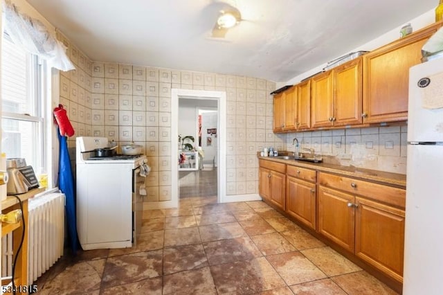 kitchen featuring radiator, a sink, white appliances, baseboards, and wallpapered walls